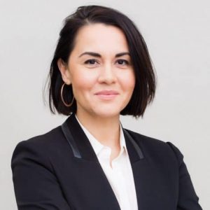 Nora Benavidez headshot (woman with short dark hair wearing a suit against a gray background)